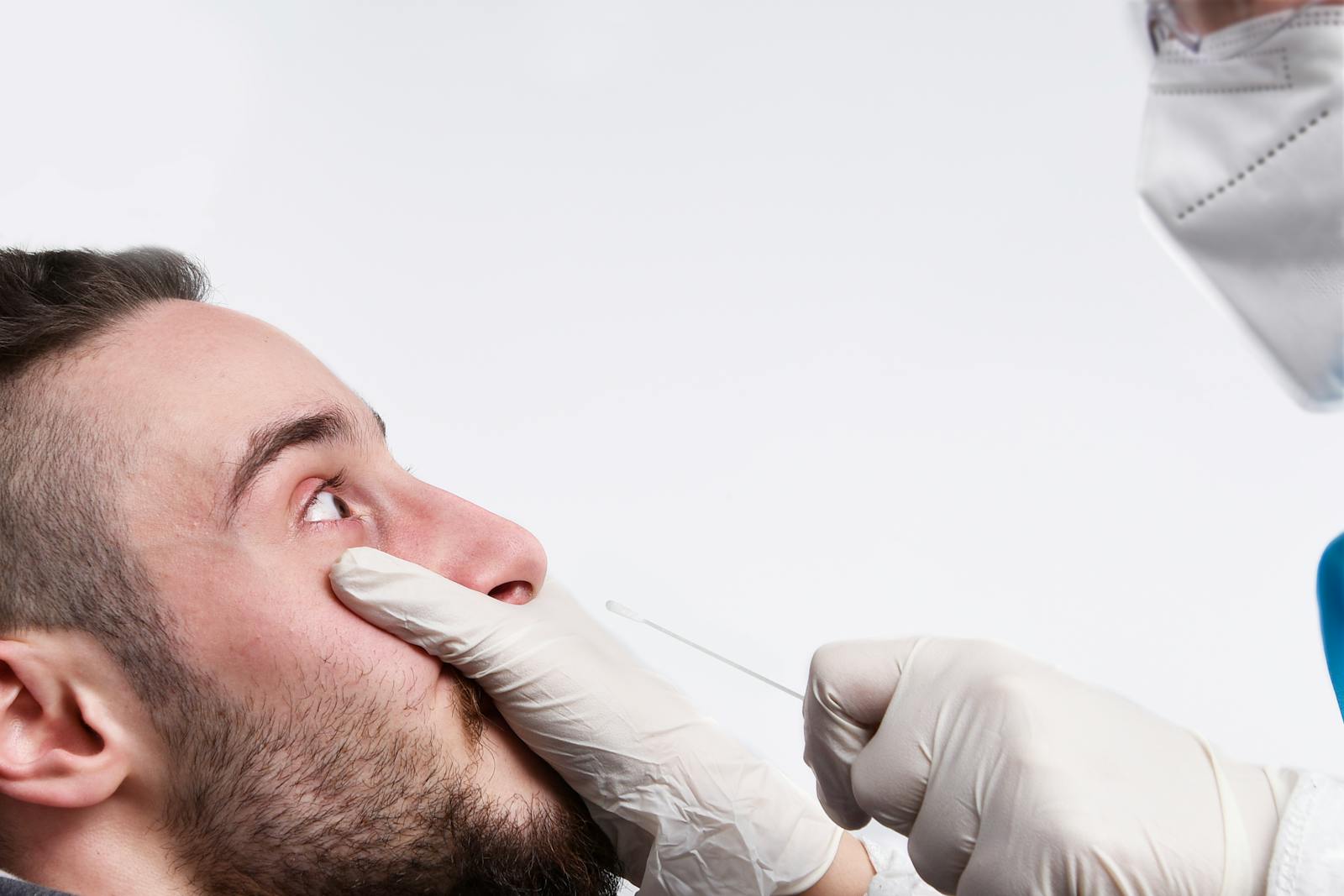 Healthcare worker giving a nasal swab test to a man on a white background.